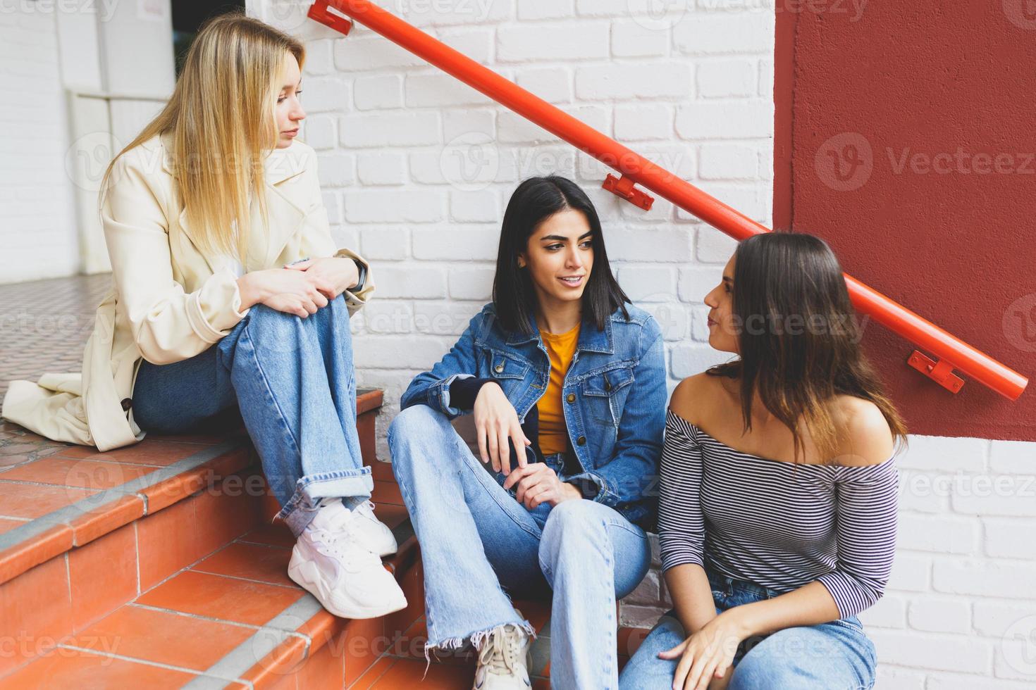 grupo multiétnico de tres amigos sentados en los escalones de la calle hablando. foto