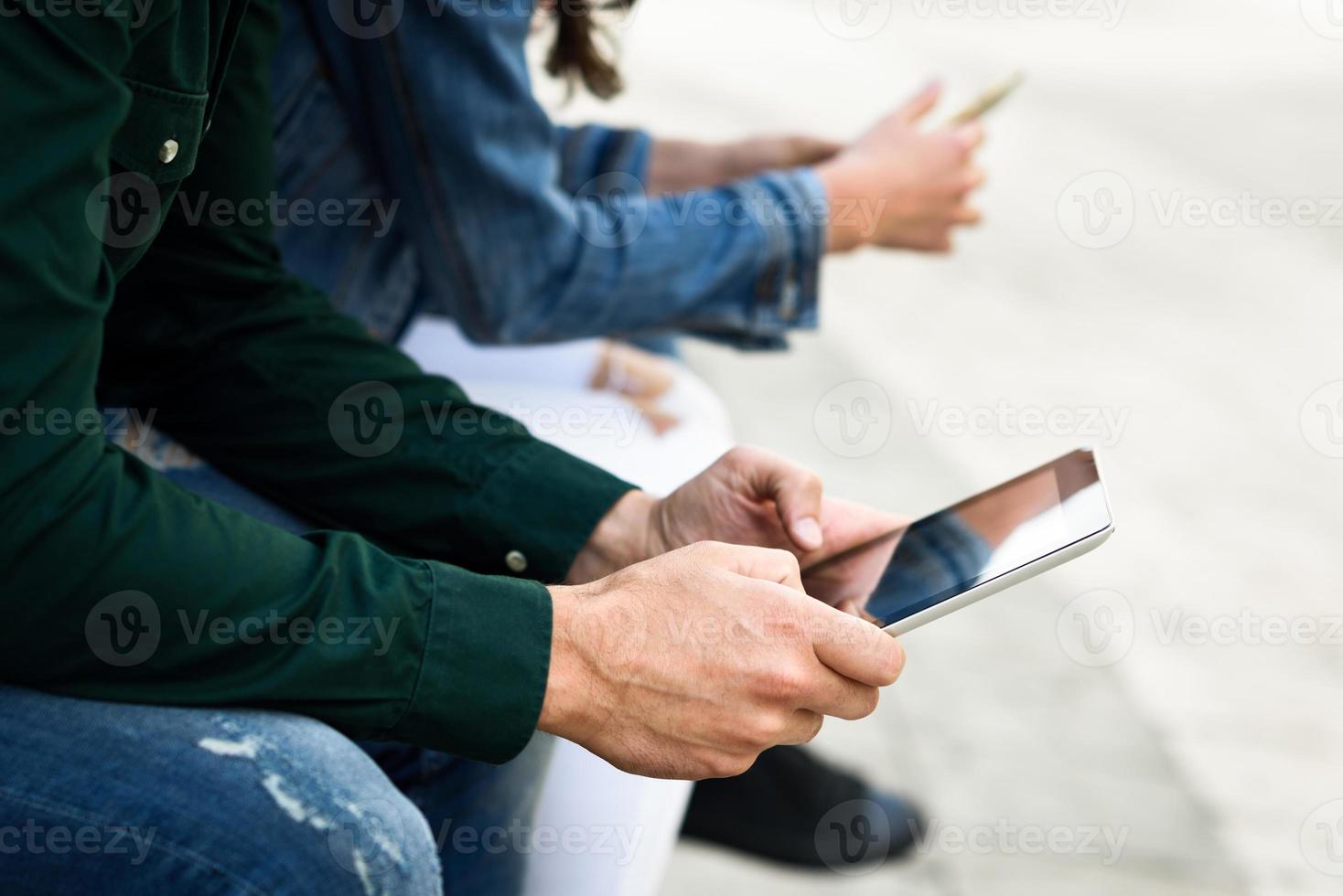 Jóvenes irreconocibles que usan teléfonos inteligentes y tabletas al aire libre foto