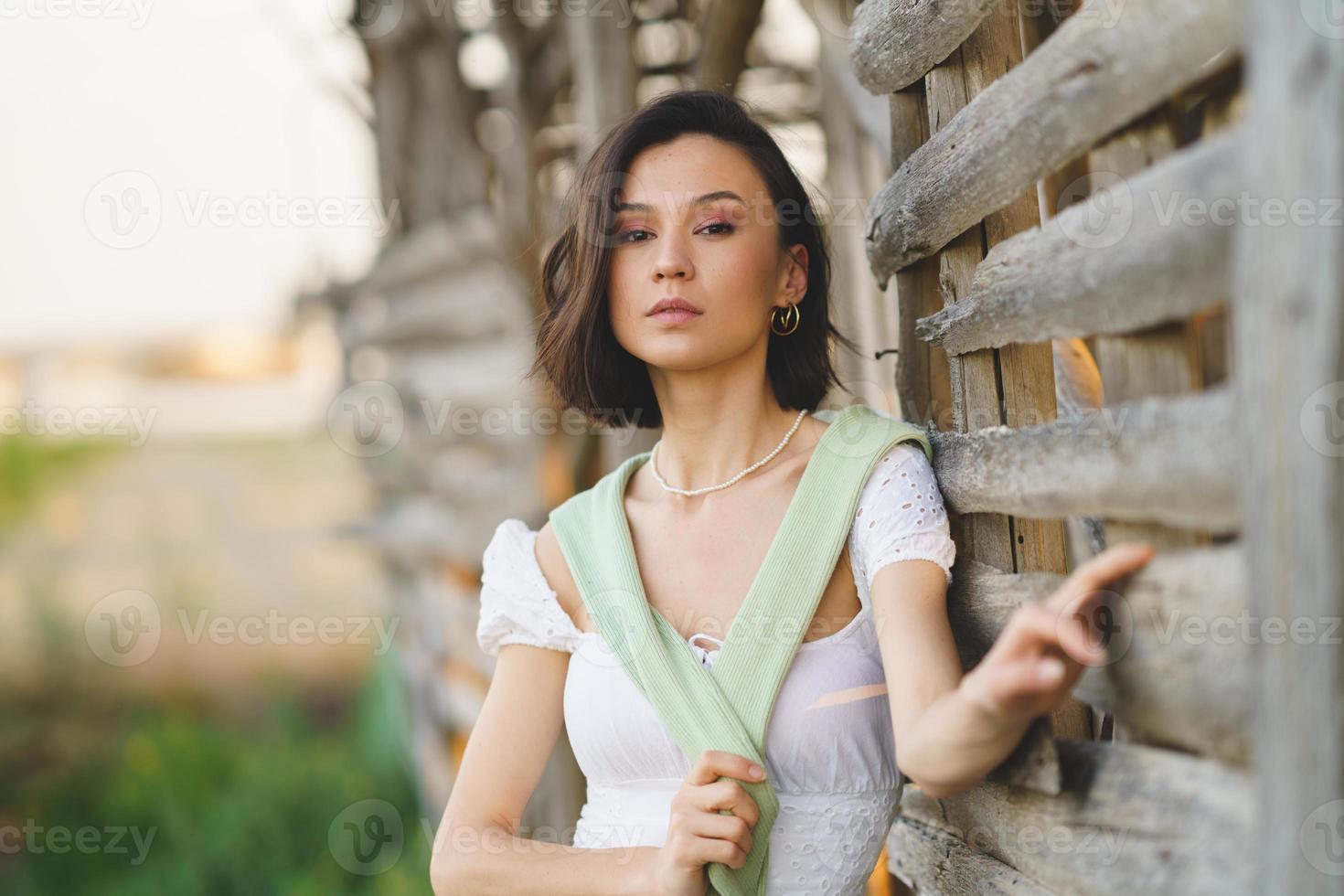 Asian woman, posing near a tobacco drying shed, wearing a white dress and green wellies. photo