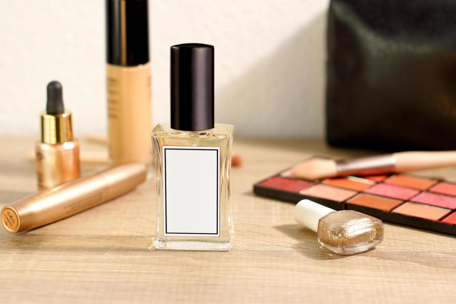 Frasco de vidrio de perfume sobre la mesa con elementos cosméticos de maquillaje, puesta en escena de estilo de vida foto