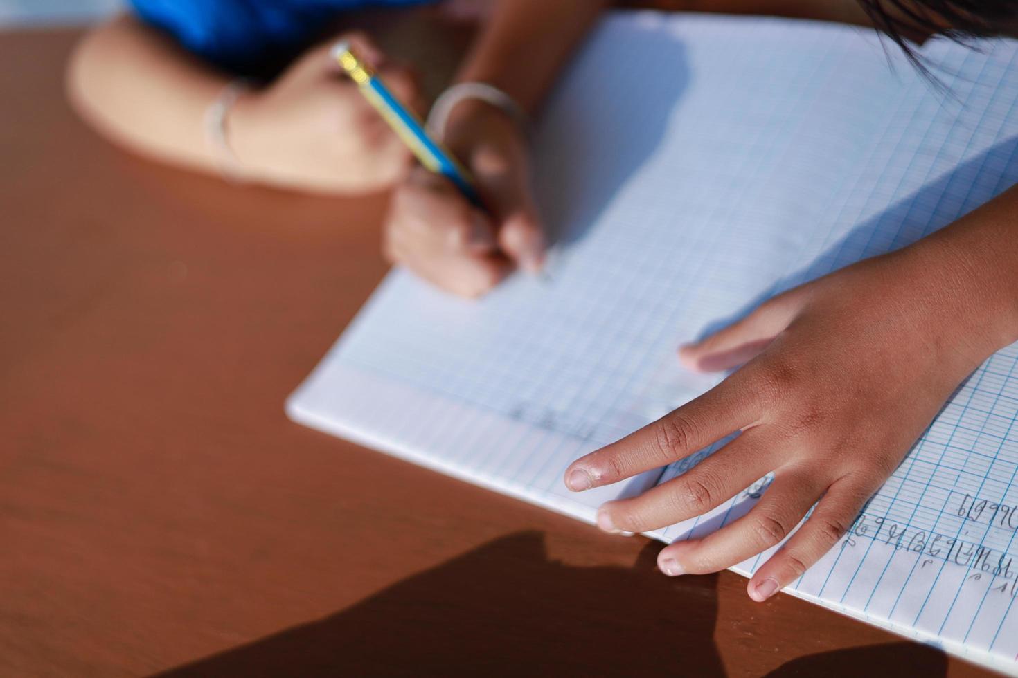 A cute little Asian girl is writing a book with a pencil on the table. photo