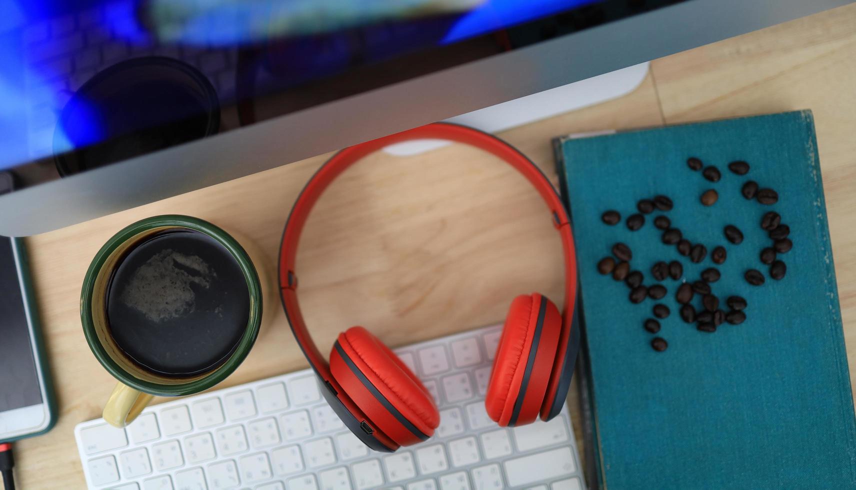 The work desk has a coffee cup and red headphones and office supplies. photo