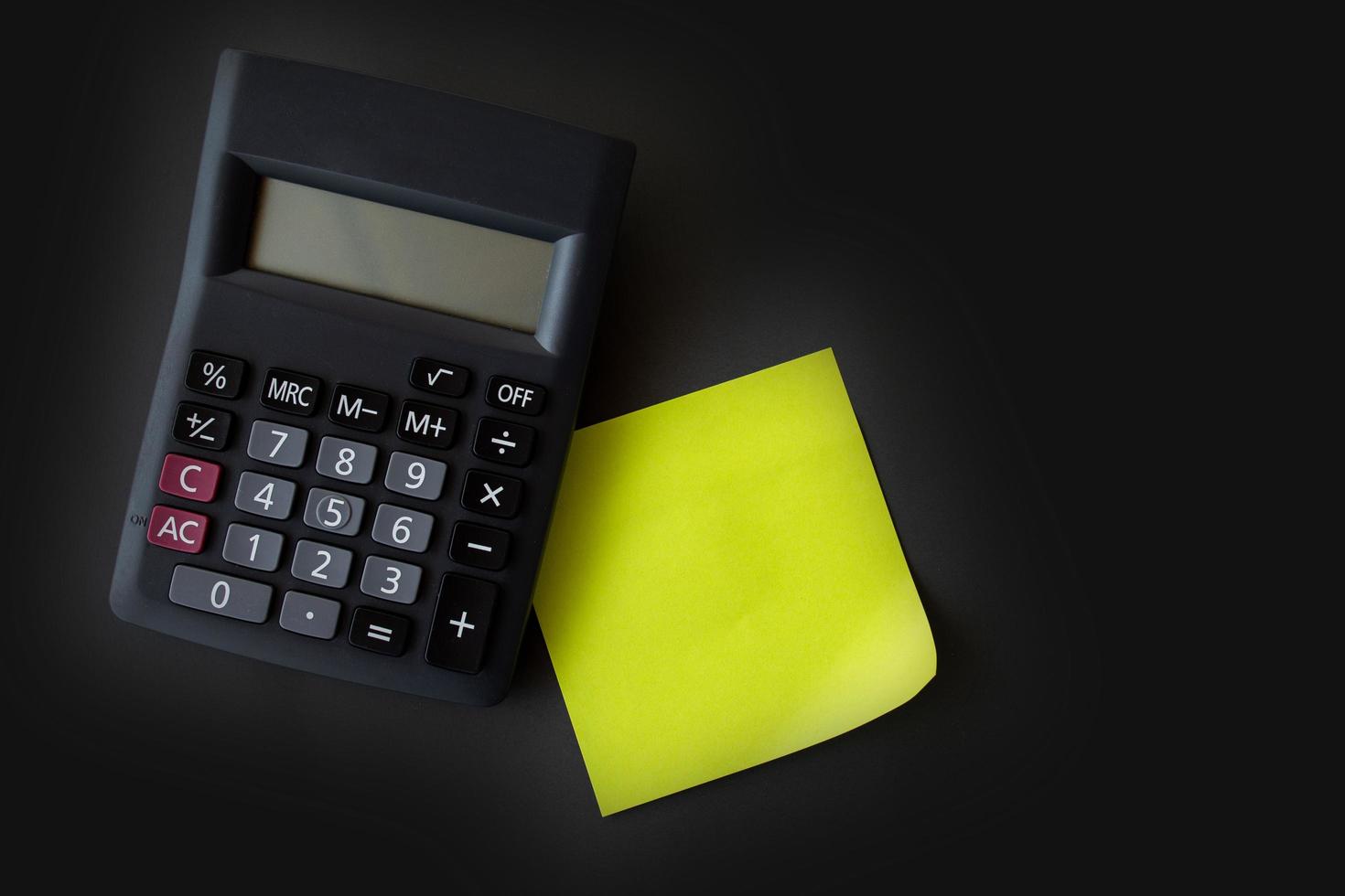 Green yellow  post-it and black calculator on gray black background. photo