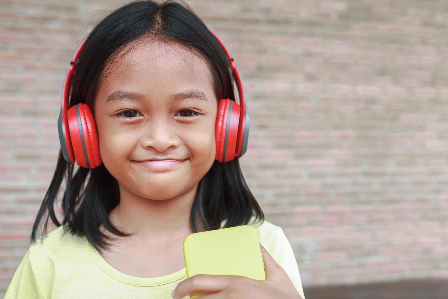 A cute Asian girl uses a red wireless headphone to listen to music on her phone photo