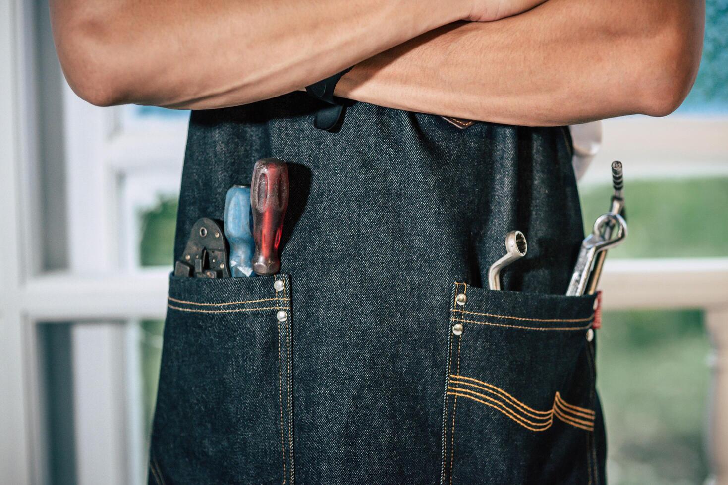 el mecánico lleva un delantal negro y hay herramientas de mano en la bolsa. foto