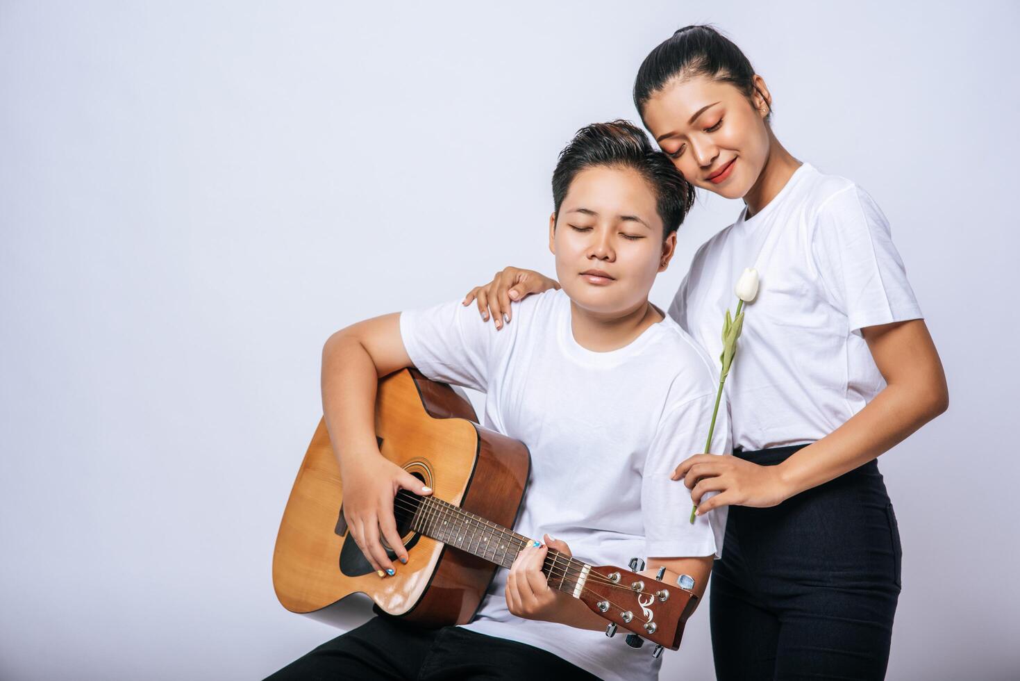 Two young women sat on a chair and played guitar. photo