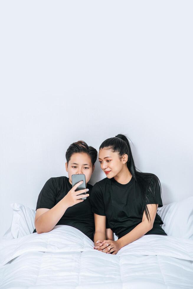 dos mujeres amorosas durmiendo y jugando teléfonos inteligentes. foto