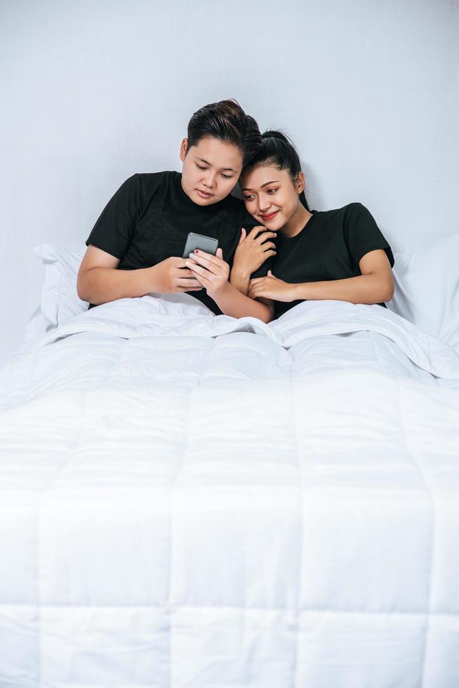 dos mujeres amorosas durmiendo y jugando teléfonos inteligentes. foto