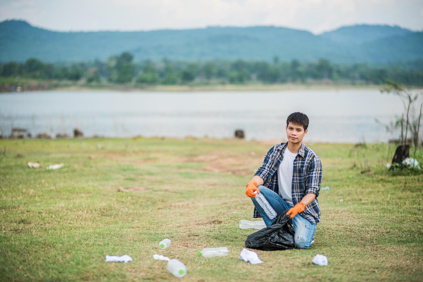 A man wearing orange gloves collecting garbage in a black bag. photo