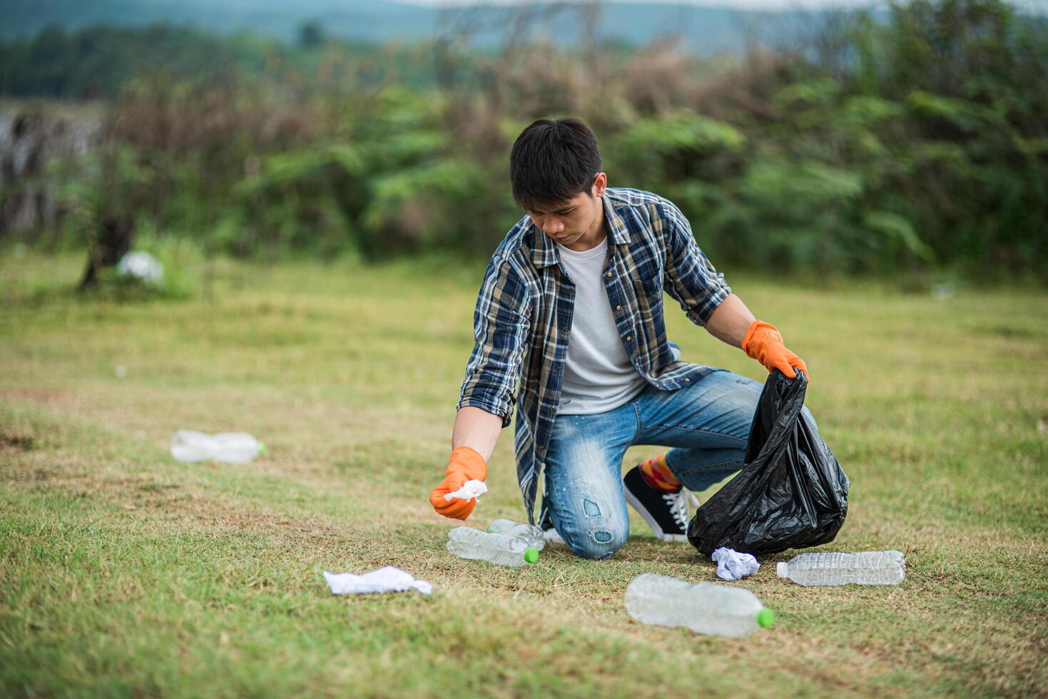 A man wearing orange gloves collecting garbage in a black bag. photo