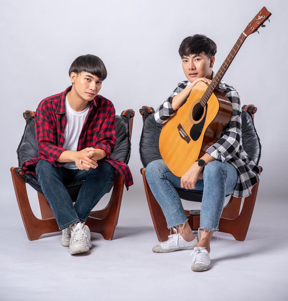 Two young men sitting in a chair holding a guitar photo