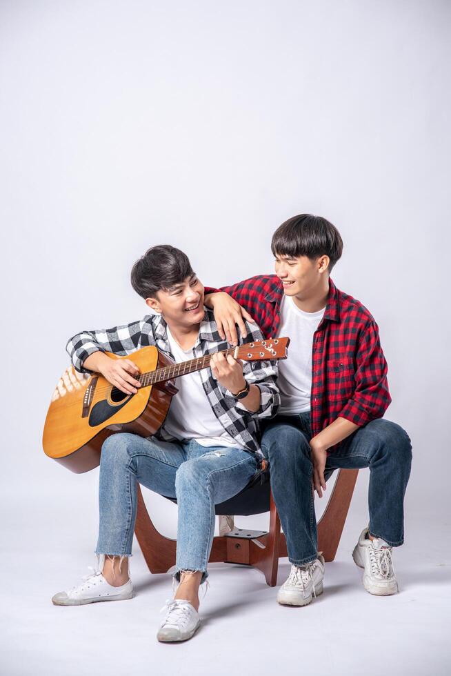 Two young men sat on a chair and played guitar. photo