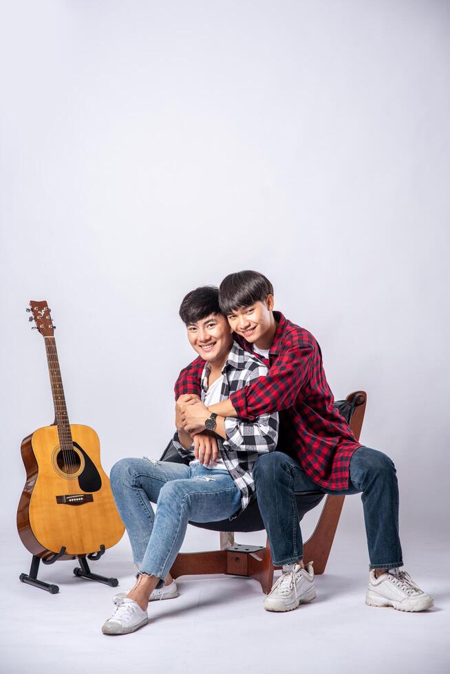 dos queridos jóvenes estaban sentados, abrazados en una silla, y con una guitarra al lado. foto