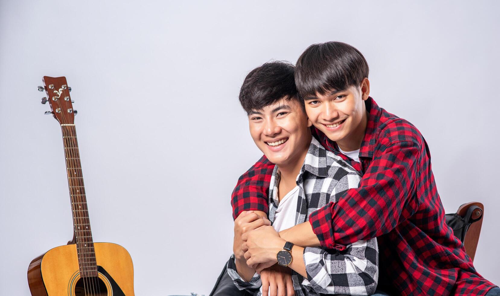 Two dear young men were sitting, cuddling in a chair, and with a guitar beside. photo