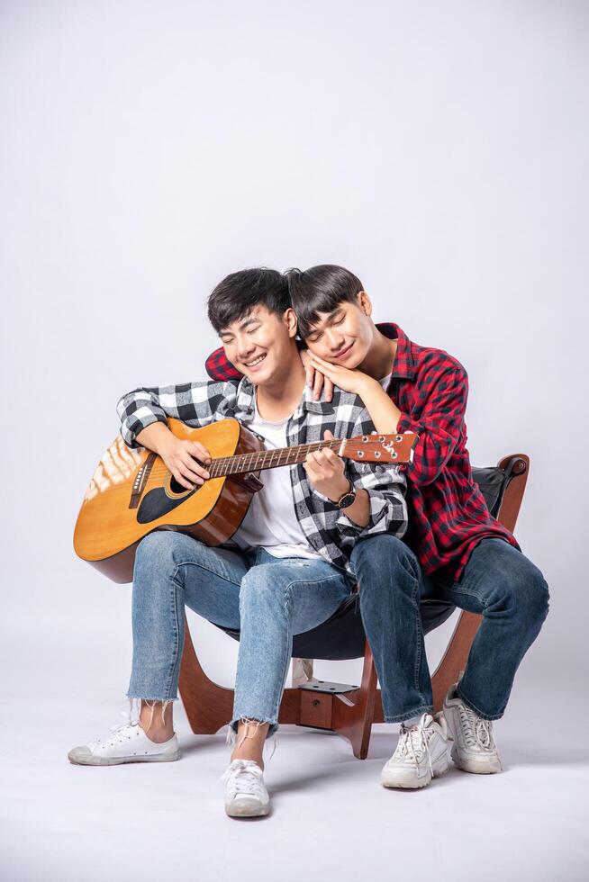 Two young men sat on a chair and played guitar. photo