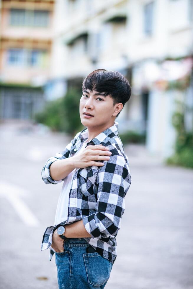 A young man in a striped shirt is standing on the street. photo