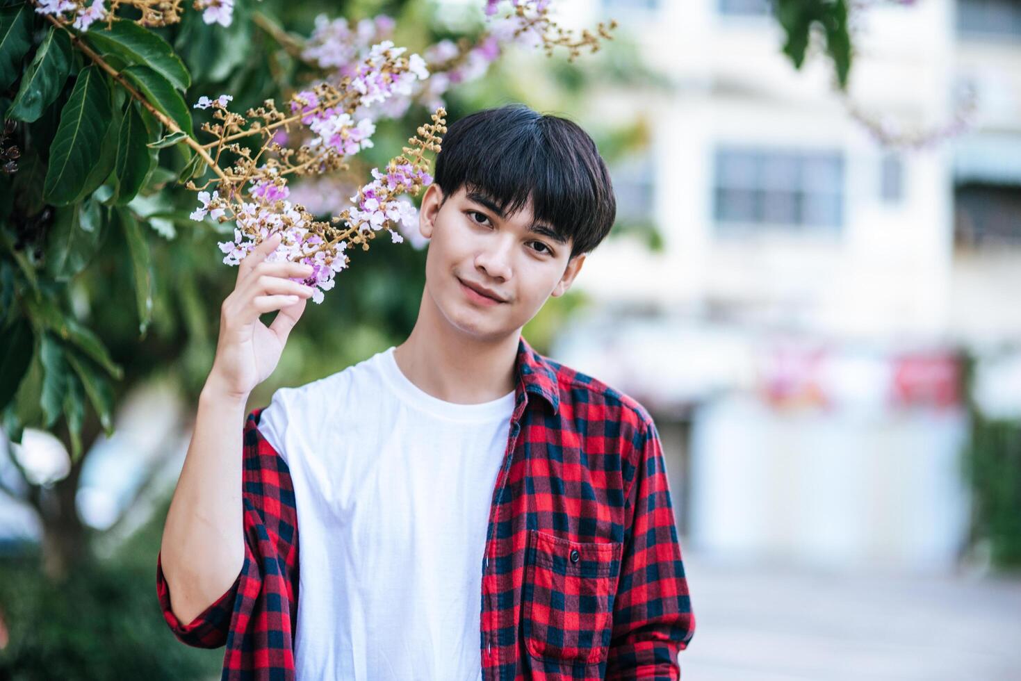 A young man in a striped shirt was standing on the roadside and holding the flower. photo