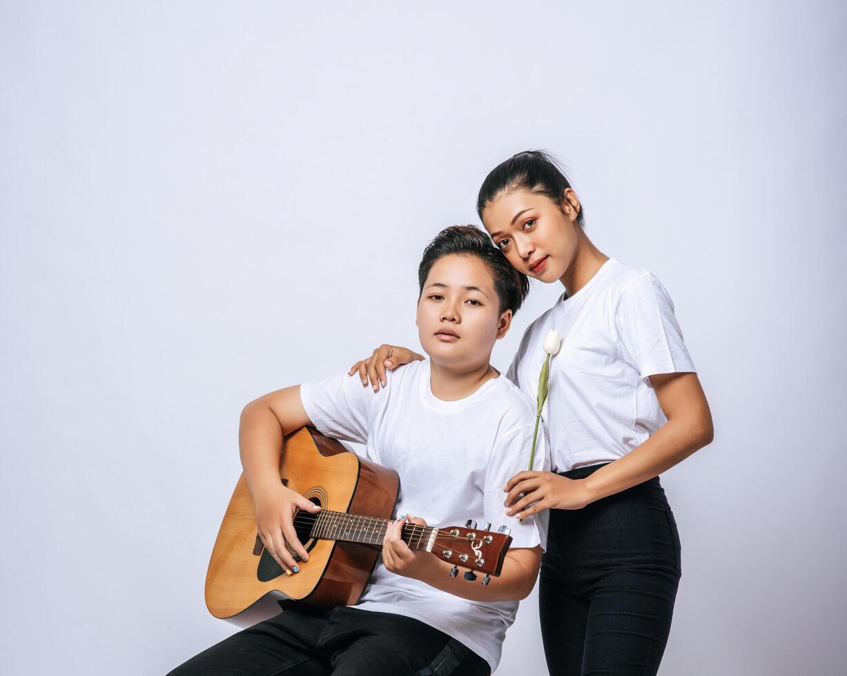 Two young women sat on a chair and played guitar. photo
