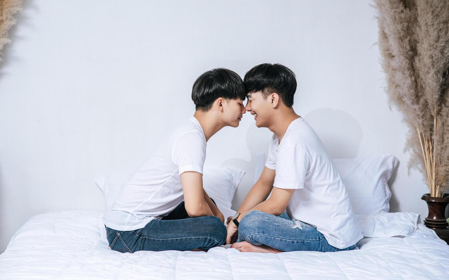 Two dear young men were sitting on the bed, holding hands and looking at each other. photo