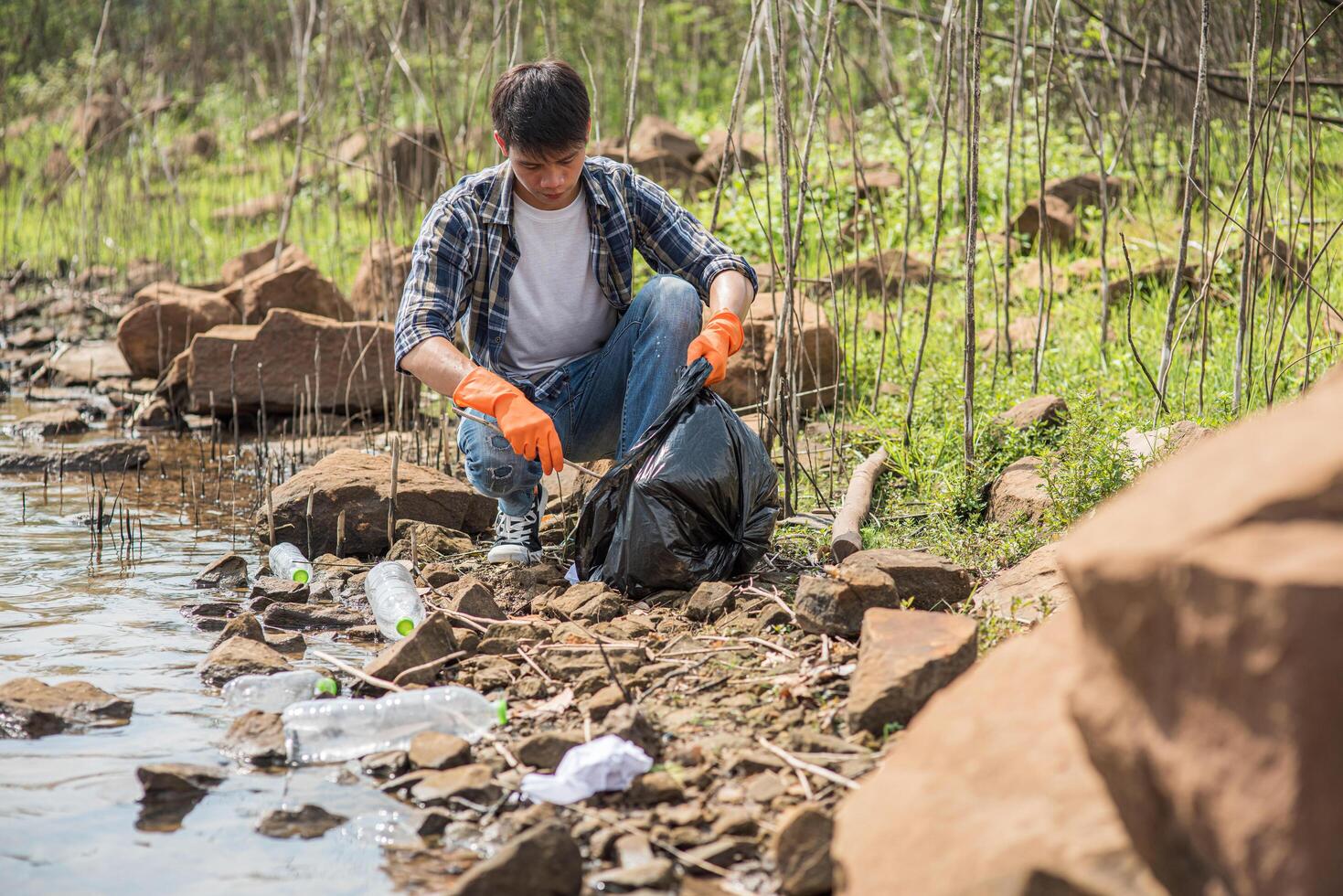 A man wearing orange gloves collecting garbage in a black bag. photo