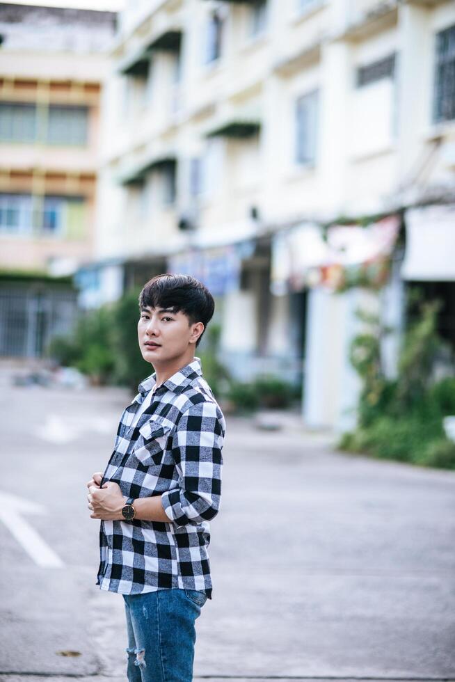 A young man in a striped shirt is standing on the street. photo