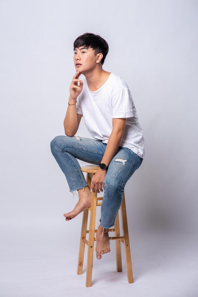 A young man in a white T-shirt is sitting on a high chair. photo