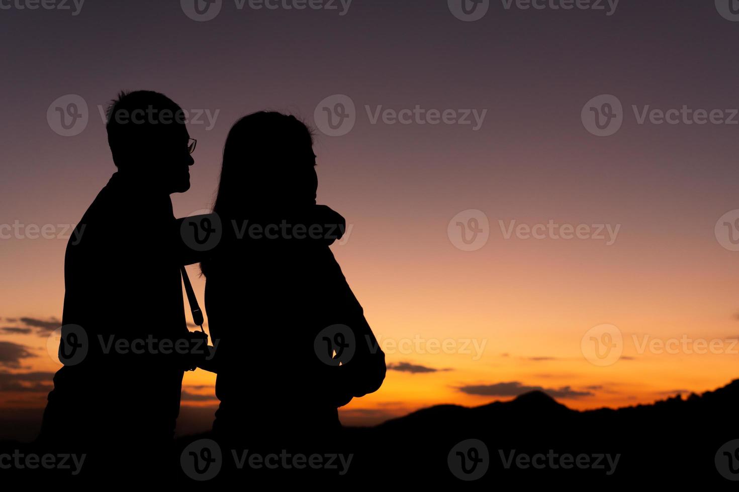 silouette de hombre y mujer como una pareja mirando el atardecer detrás de la montaña foto