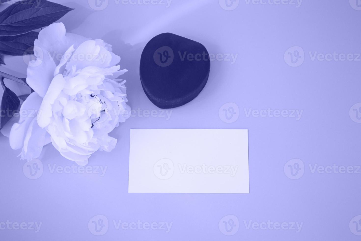 Close up of a greeting card mockup. On a very peri background, a business card, a red jewelry box and a white peony. Top view photo