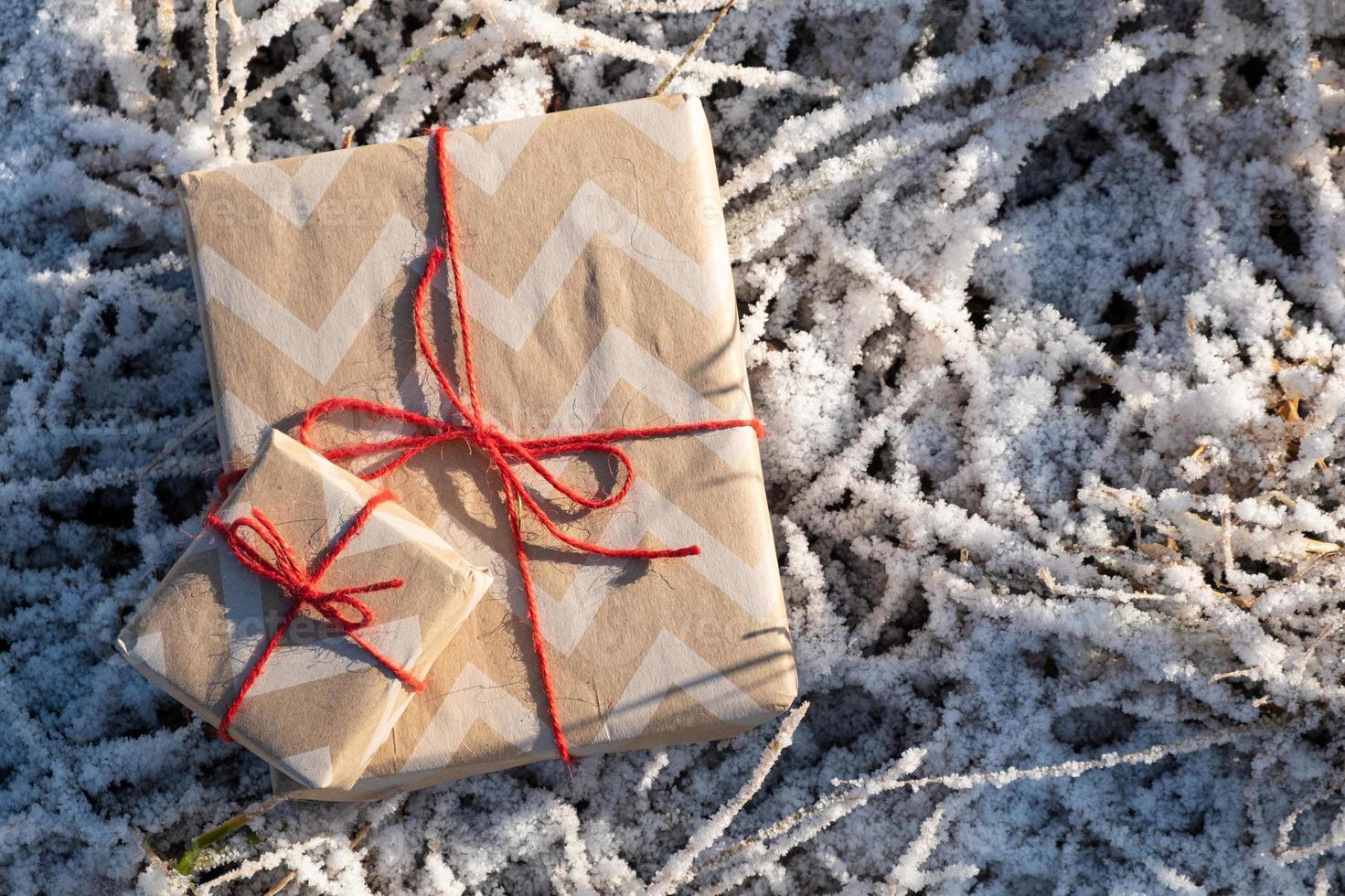 Cajas de regalo atadas con hilo rojo sobre la hierba helada, felicitación y celebración de las fiestas. foto