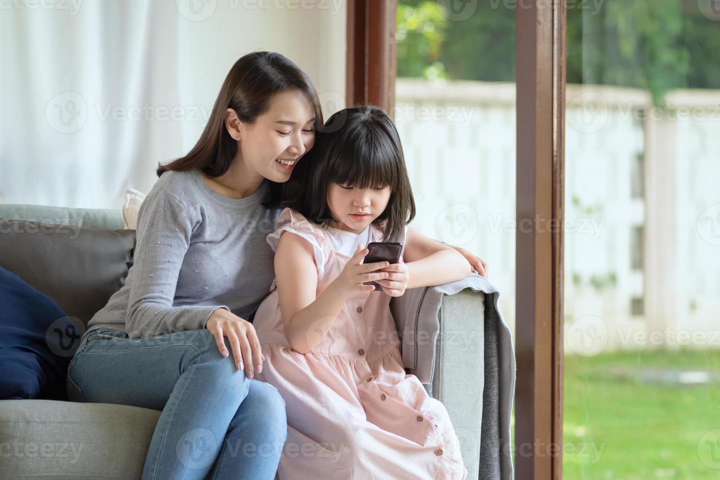 Madre asiática y su hija disfrutan de usar Internet a través de teléfonos inteligentes en casa foto