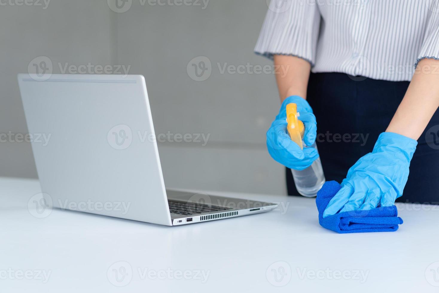 Mujer de negocios con máscara y desinfectante personal para limpiar su mesa en la oficina para mantener la higiene. preventiva durante el período de epidemia de coronavirus o covid19. foto