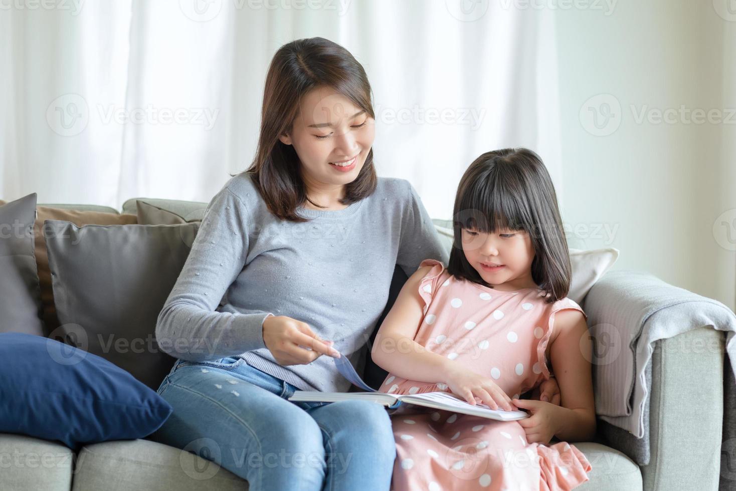 Happy asian mother teaching her cute kid daughter to studying in living room at home photo