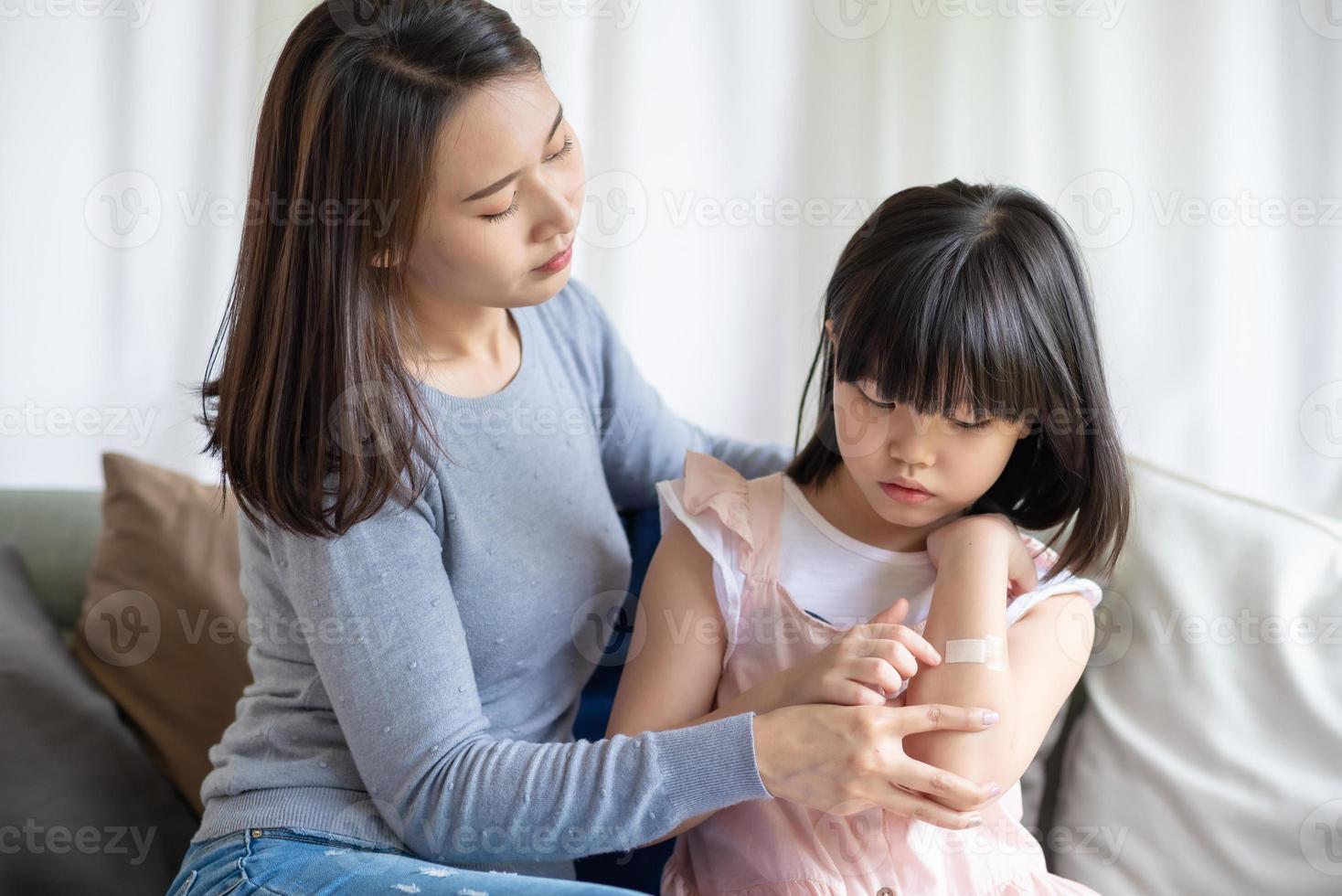 Madre asiática poniendo corte vendaje adhesivo de yeso a su hija en casa foto