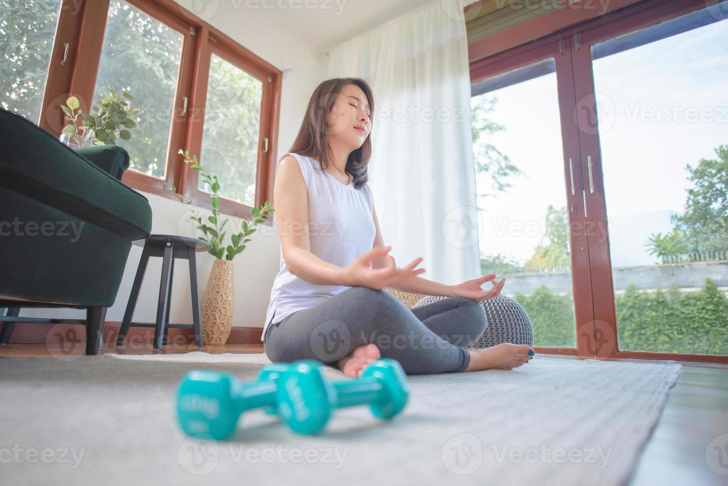 Beautiful asian woman keep calm and meditates while practicing yoga at home for healthy trend lifestyle photo