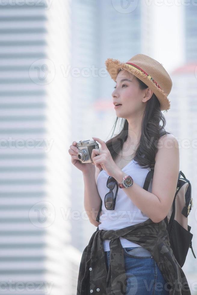 Hermosa mujer turista asiática en solitario disfruta tomando fotos con una cámara retro en un lugar turístico. viajes de vacaciones en verano.