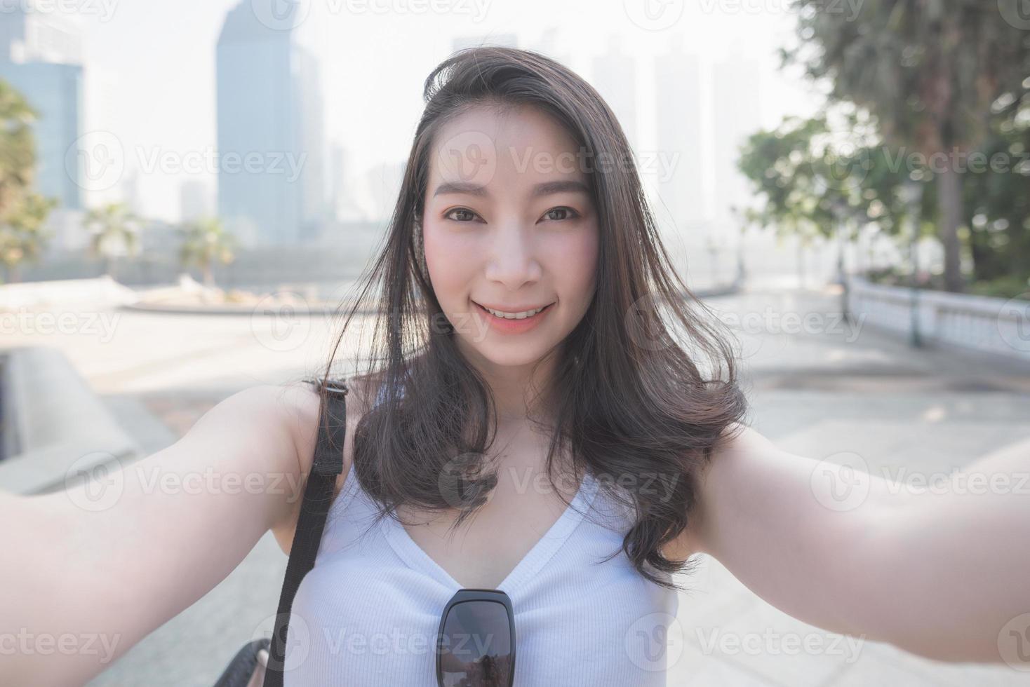 Beautiful asian solo tourist woman taking selfies on a camera in urban city downtown. Vacation travel in summer. photo