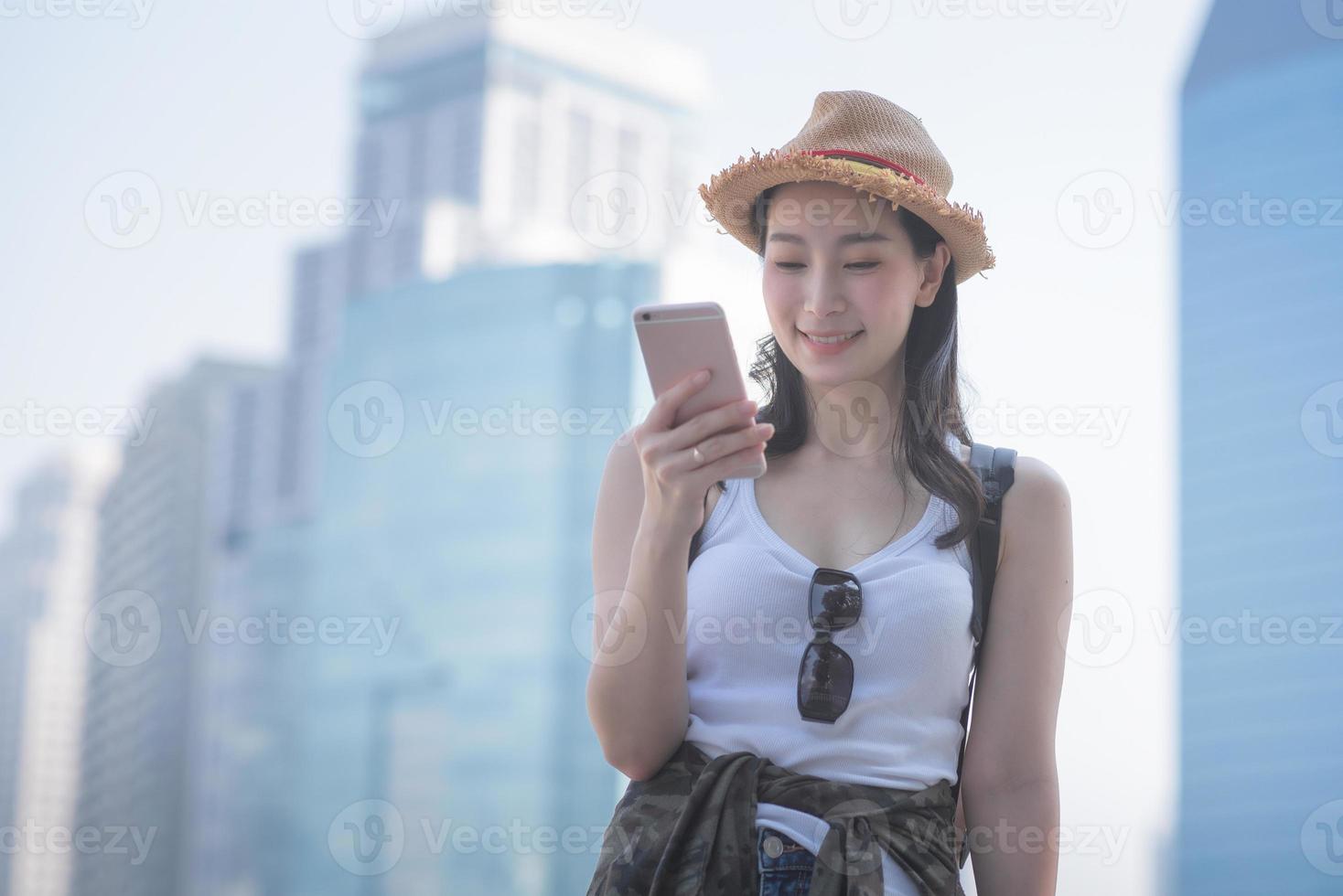 Beautiful asian solo tourist woman smiling and looking at mobile phone for searching tourists sightseeing spot. Vacation travel in summer photo