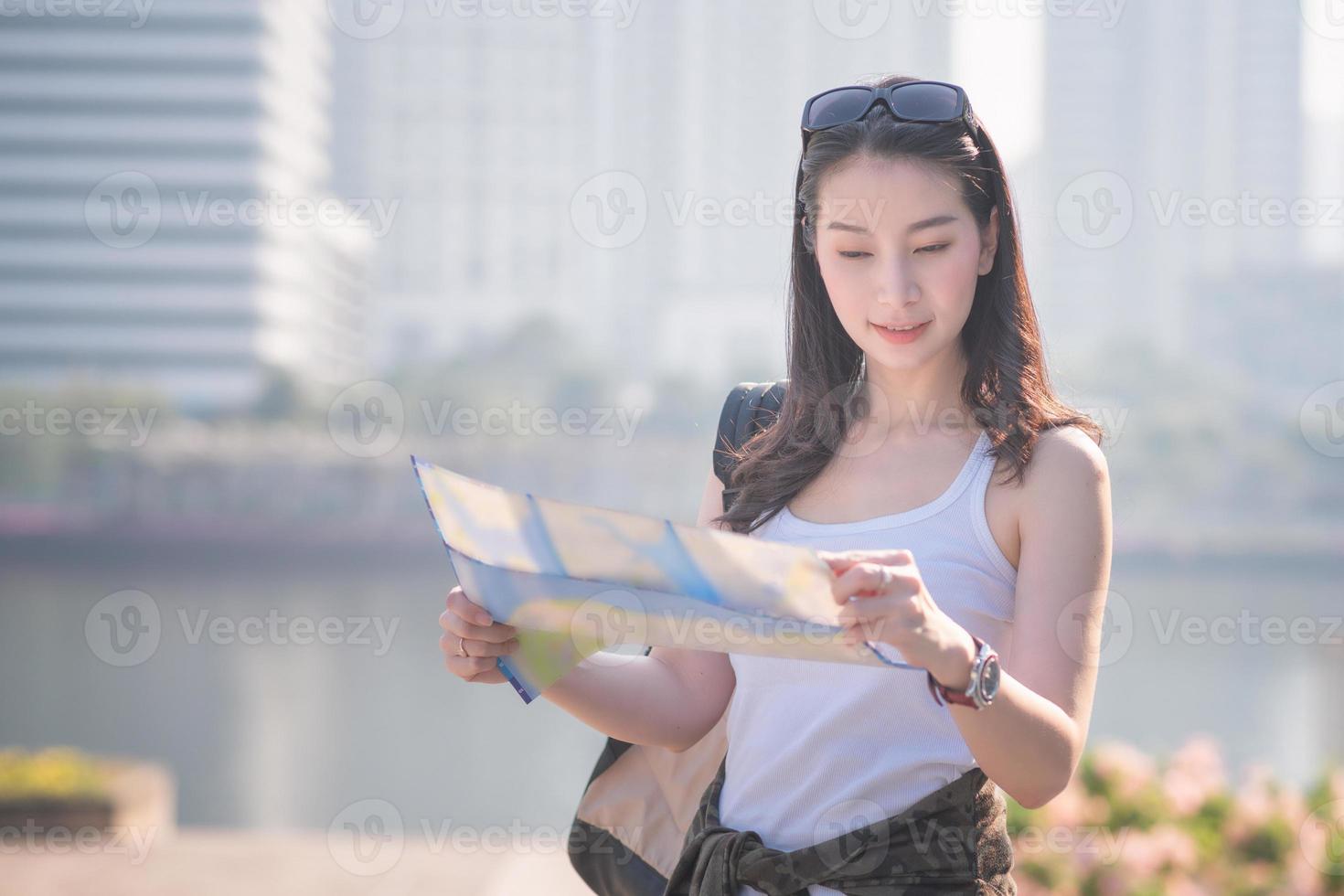 hermosa mujer asiática turista en solitario mirando el mapa en busca de turistas lugares de interés turístico. viajes de vacaciones en verano. foto