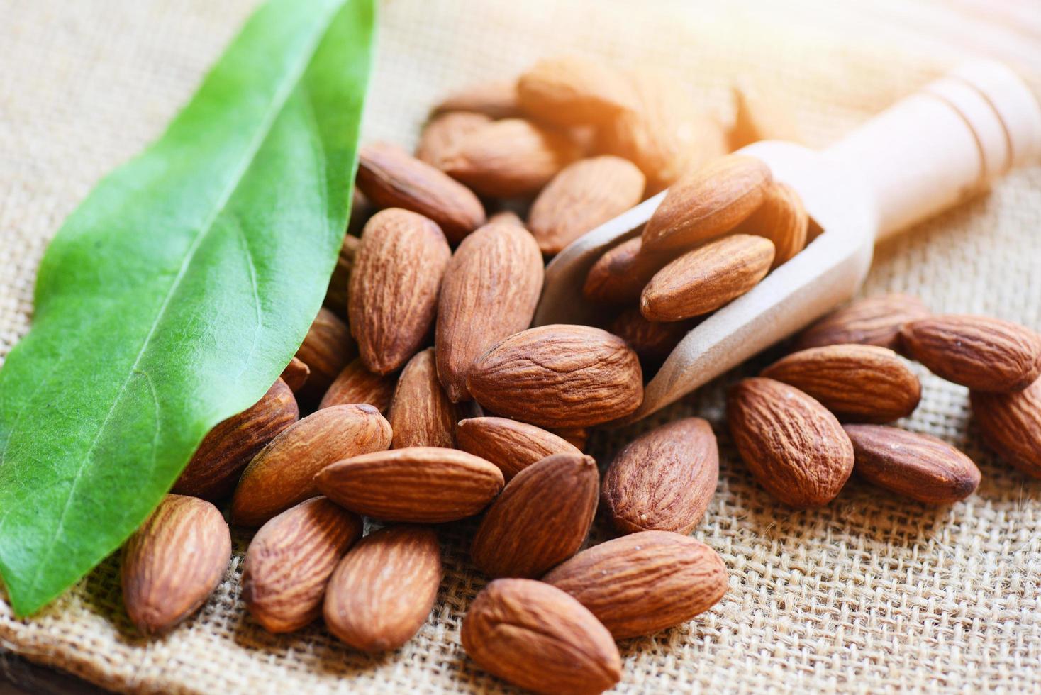 Almendras en cuchara de madera y fondo de saco, vista superior sobre la mesa, cerca de almendras tostadas, nueces, proteína natural, alimento y para bocadillos foto