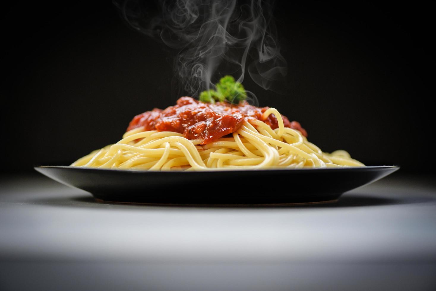 Spaghetti italian pasta served on black plate with tomato sauce and parsley in the restaurant italian food and menu concept - spaghetti bolognese on black background photo