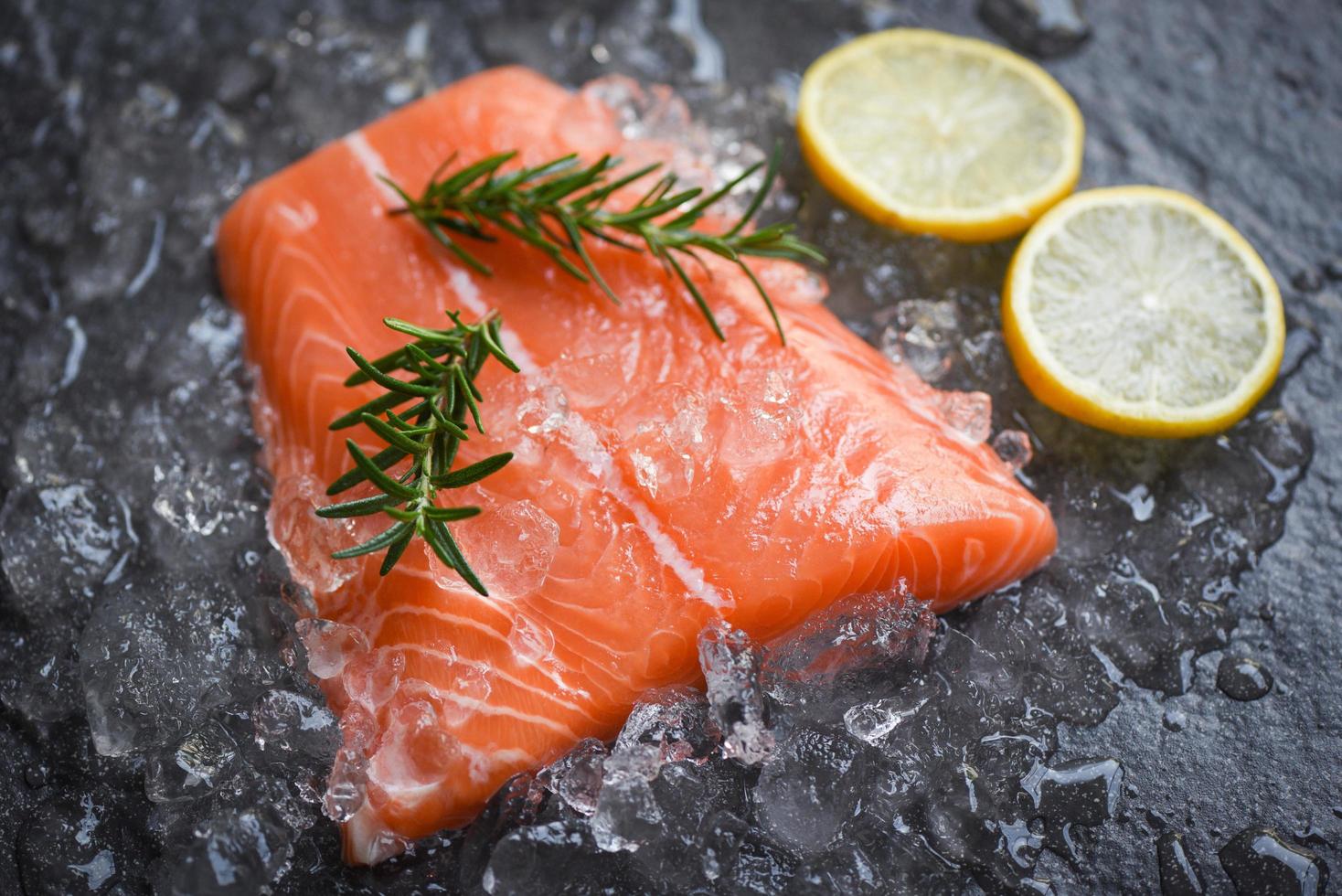 Filete de pescado de salmón crudo fresco sobre hielo con comida de romero limón y fondo de piedra oscura foto