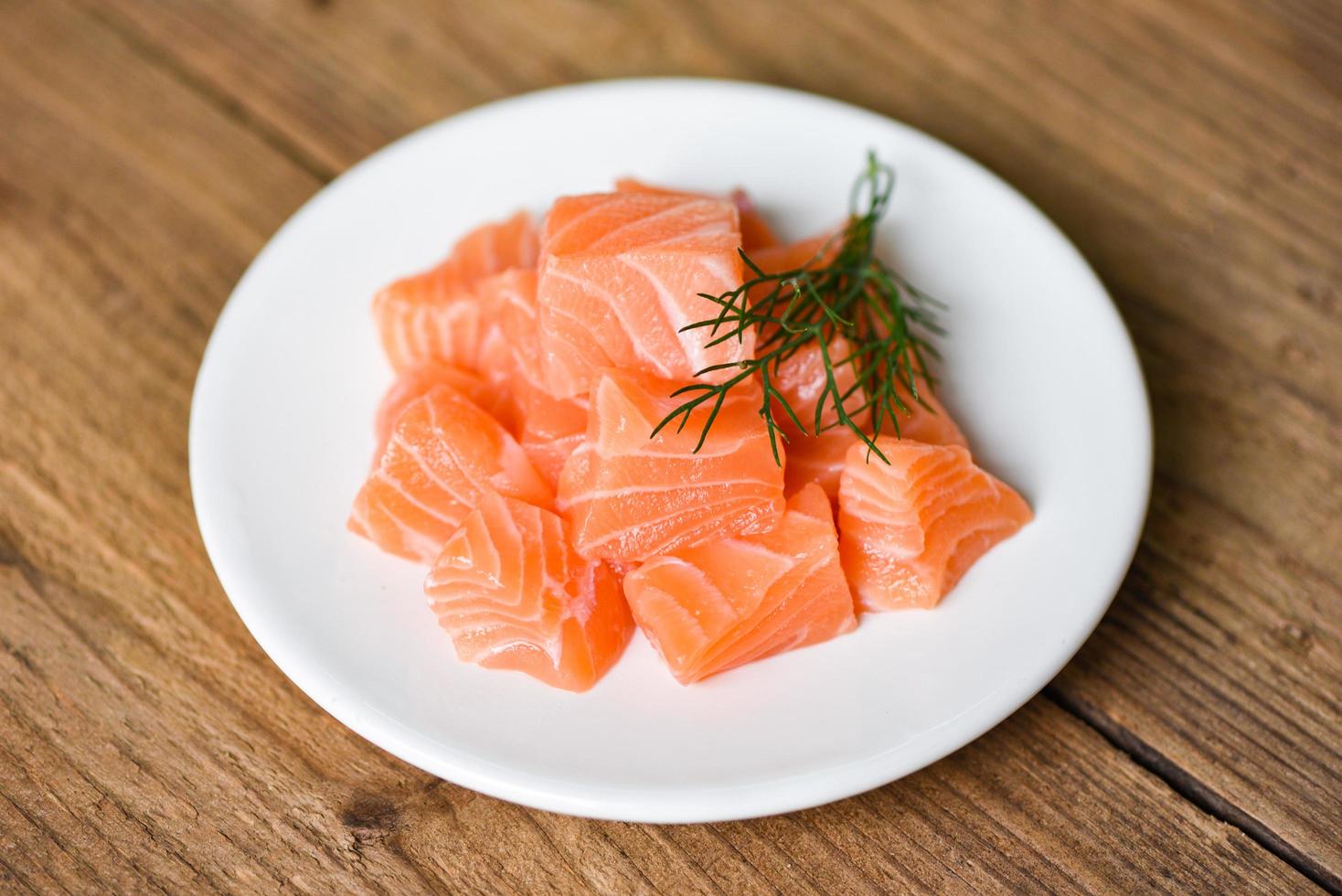 Cubo de filete de salmón crudo con hierbas y especias en un plato blanco sobre fondo de madera foto