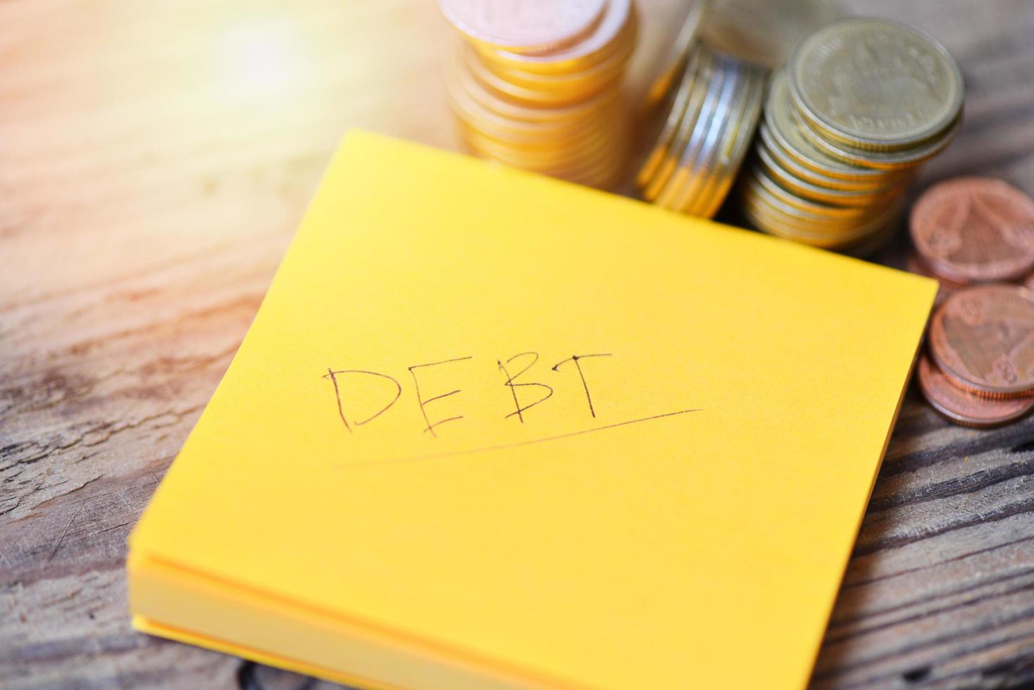 Debt concept with write debt on paper and stacked coins on wooden table background photo