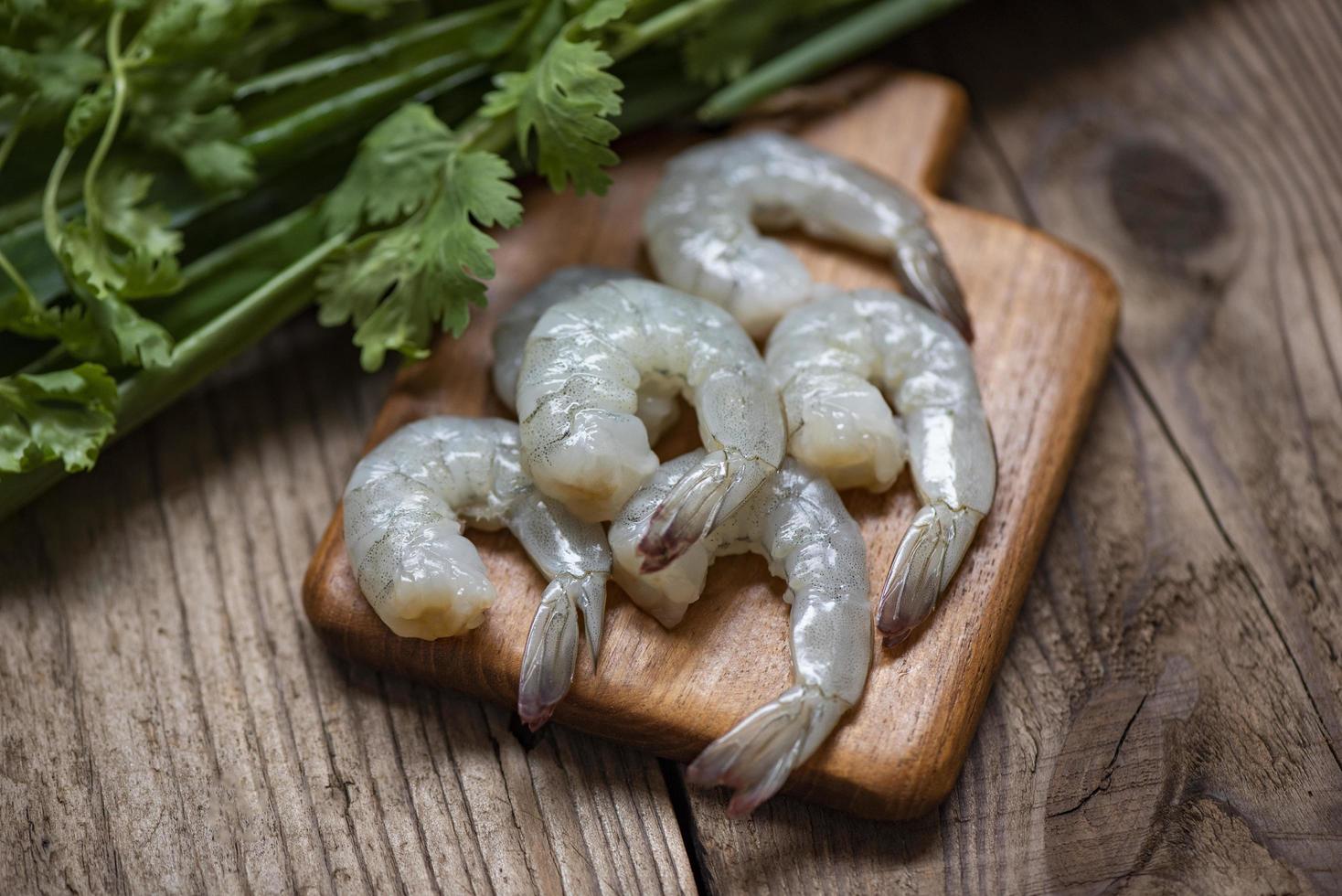 Camarones crudos sobre tabla de cortar de madera de fondo para cocinar - cerrar camarones frescos o langostinos, mariscos en estantería foto