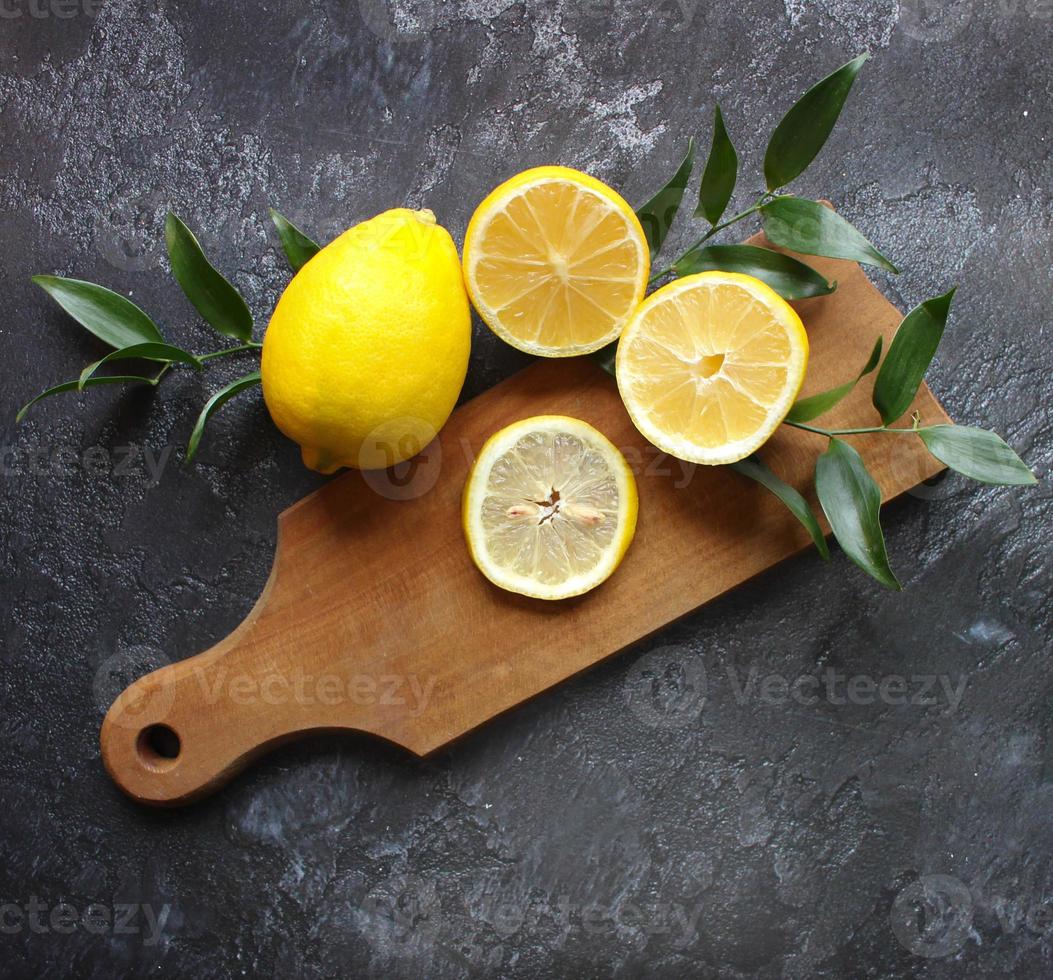 Lemons and green leaves on bright black background. Top view flat lay copy space. Lemon fruit citrus minimal concept vitamin C. photo