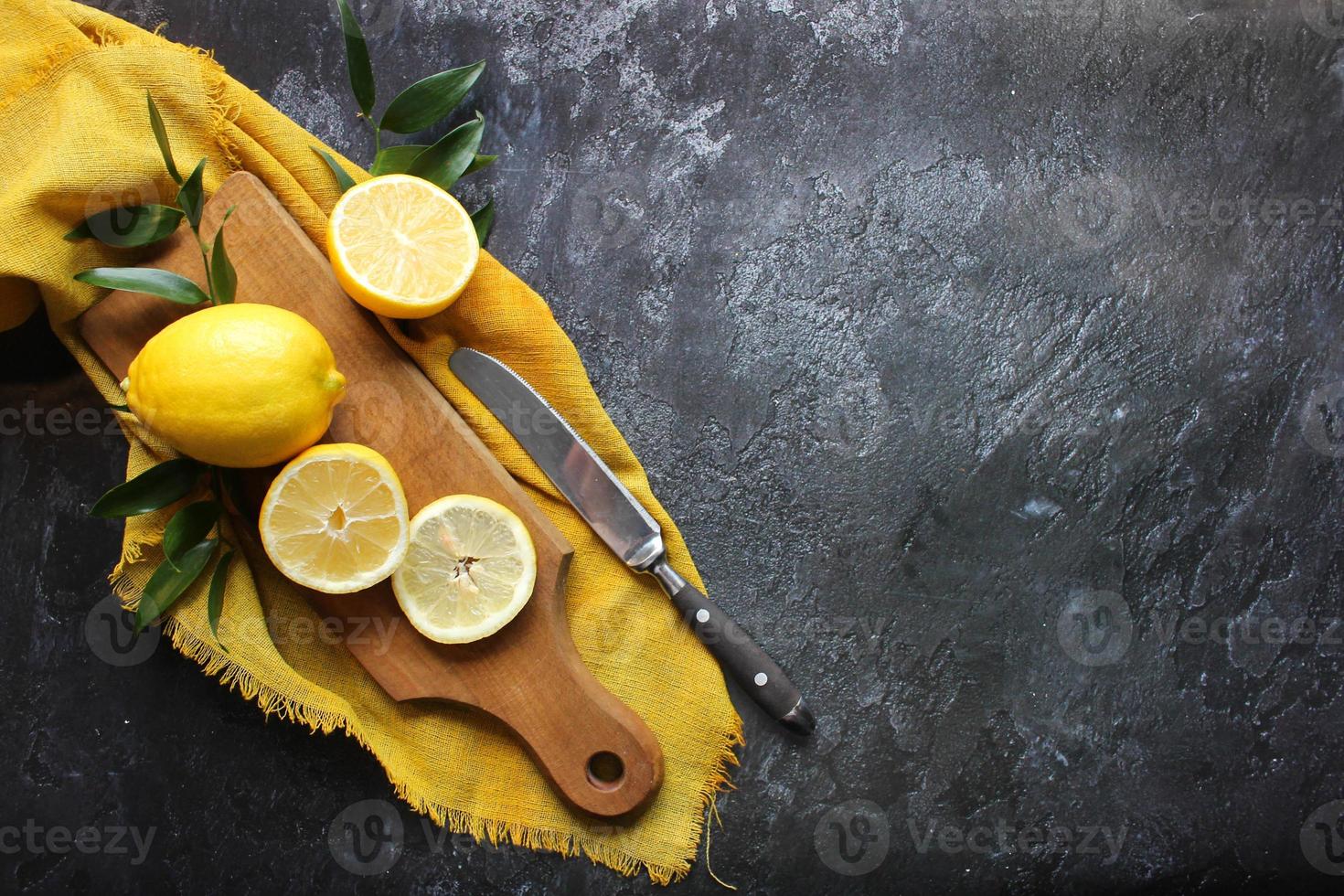 Lemons and green leaves on bright black background. Top view flat lay copy space. Lemon fruit citrus minimal concept vitamin C. photo