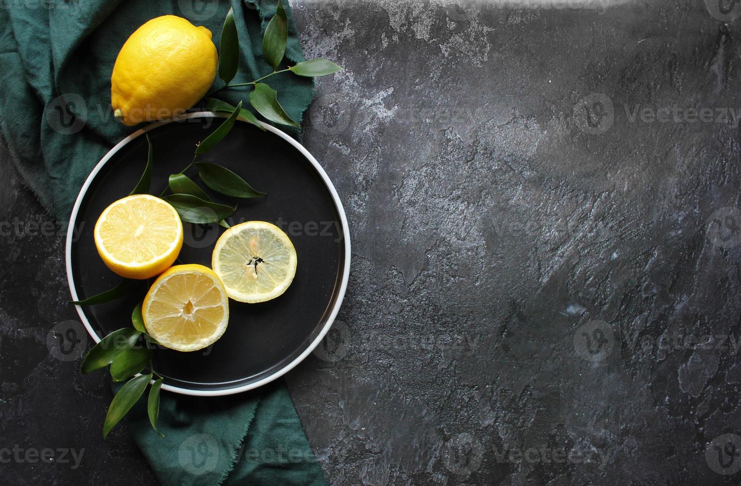 Lemons and green leaves on bright black background. Top view flat lay copy space. Lemon fruit citrus minimal concept vitamin C. photo