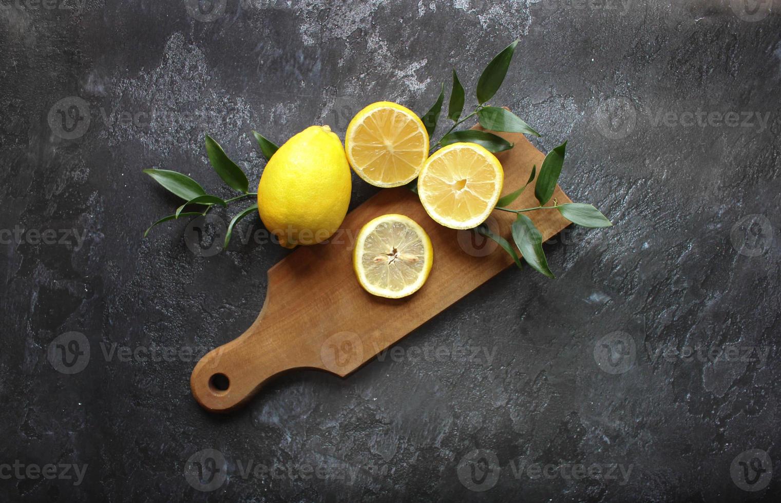 Lemons and green leaves on bright black background. Top view flat lay copy space. Lemon fruit citrus minimal concept vitamin C. photo