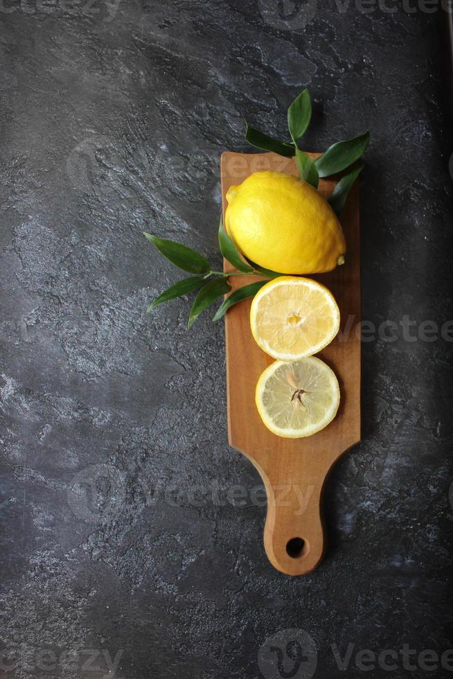 Lemons and green leaves on bright black background. Top view flat lay copy space. Lemon fruit citrus minimal concept vitamin C. photo