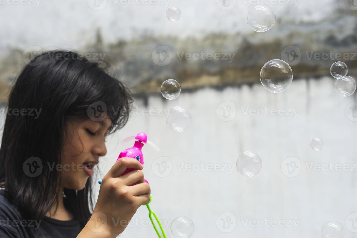 una niña que sostiene una máquina de hacer burbujas y las sopla. foto